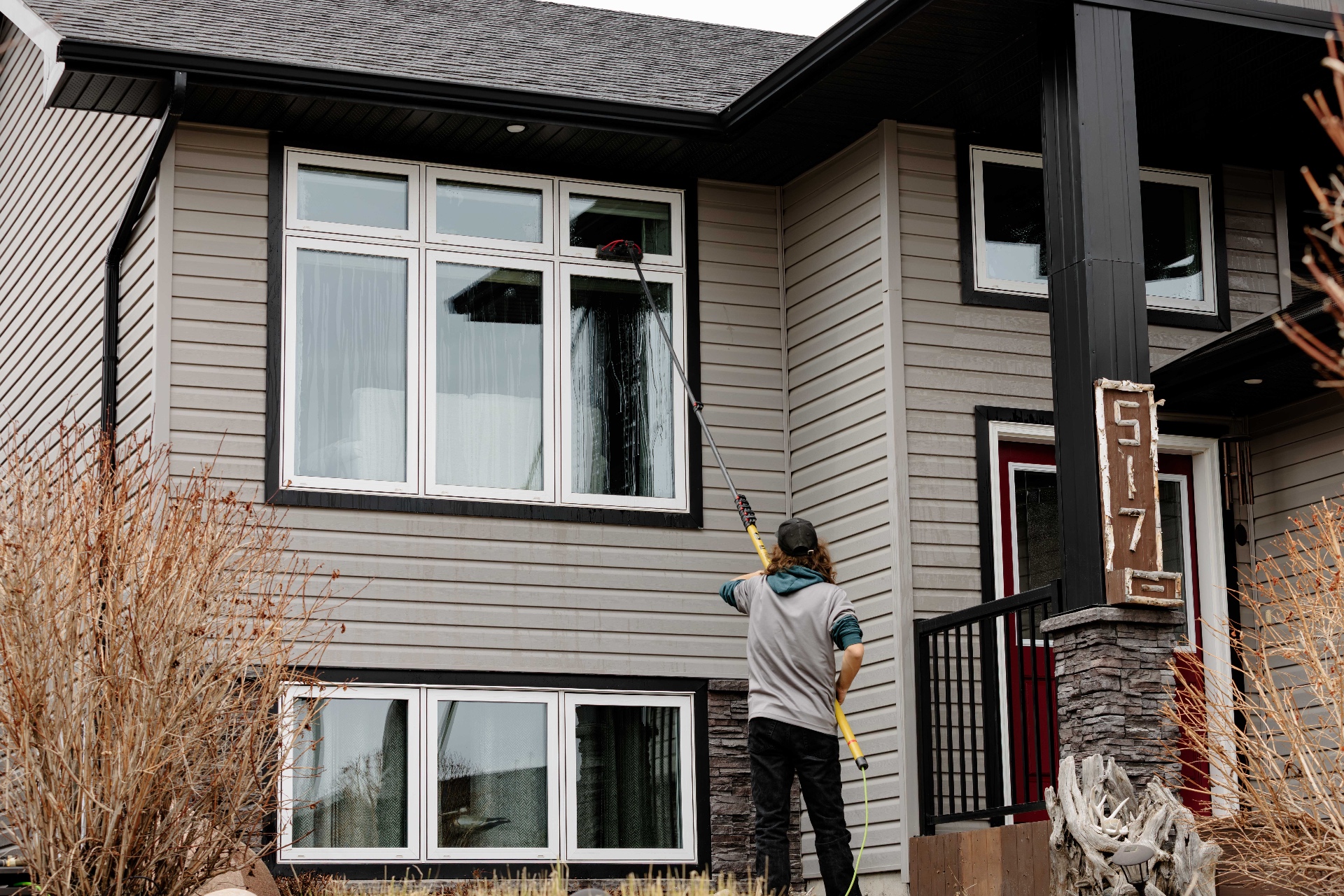 Clear Windows technician cleaning upper exterior windows on a modern home
